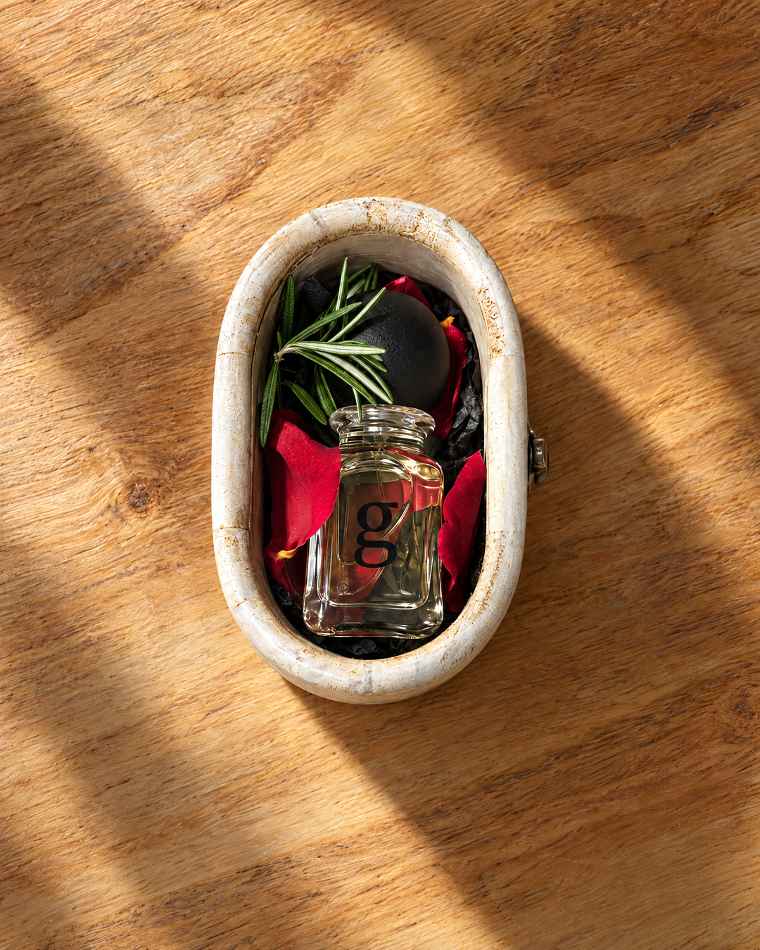 Rose Nebula perfume bottle aligned straight inside its oval wooden packaging, viewed from above on a wood table.